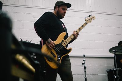 Young man playing guitar against wall