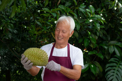 Man holding durian while standing against plants