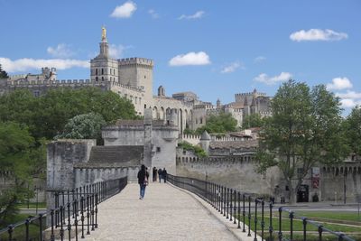 People walking in front of historical building against cloudy sky