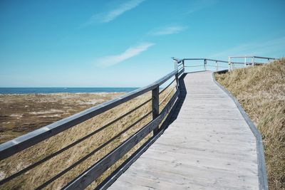 Boardwalk leading towards sea against clear sky