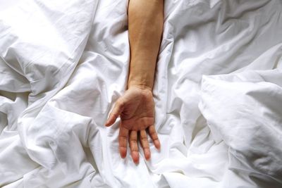 Cropped image of man hand on crumpled blanket at bed