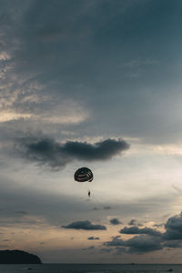 Low angle view of person in parachute over sea during sunset against cloudy sky