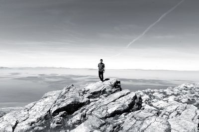 Full length of mid adult man standing on rock by sea against sky