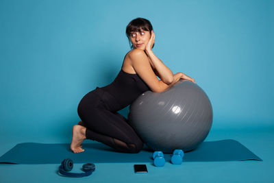 Portrait of young woman exercising against blue background