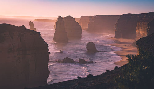 Rock formations on beach against sky during sunset