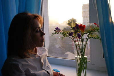 Woman looking at flower vase against window at home