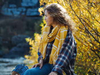 Pretty curly woman in plaid shirt sitting with a yellow tree on a background 