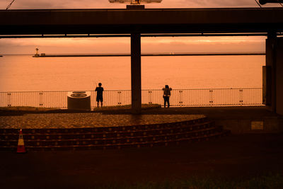 Silhouette people standing by sea against sky during sunset