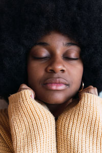 Portrait of cheerful young african american female with afro hairstyle on a gray background with his hands hidden in his sweater resting on his face while looking at camera