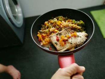 Cropped hand of person holding pasta in cooking pan at home