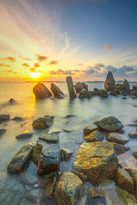 Rocks on beach against sky during sunset