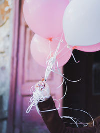 Close-up of hand holding balloons against pink door