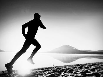 Silhouette man by lake against clear sky