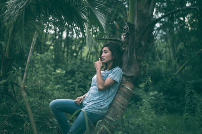 Young woman sitting on tree trunk in forest