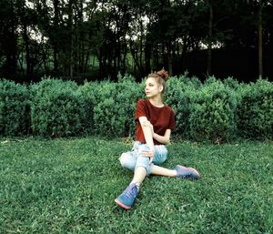 Young woman sitting on grassy field against trees