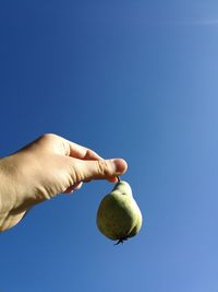 Low angle view of hand holding banana against clear blue sky