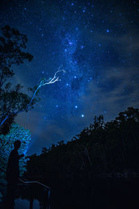 Silhouette man standing by lake against star field at night