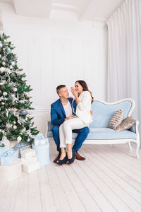 Couple sitting on sofa by christmas tree at home