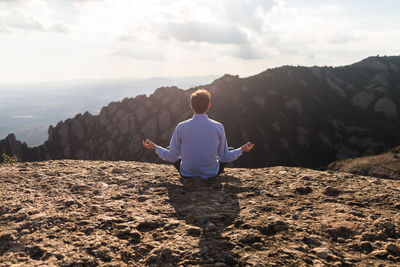 Rear view of man doing yoga on mountain against sky