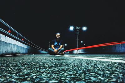 Full length of young man sitting on street at night