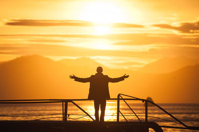 Silhouette man standing by sea against sky during sunset