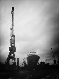 Cranes at harbor against cloudy sky