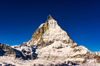 Low angle view of snowcapped mountain against clear blue sky