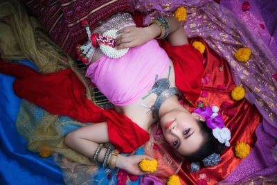 Smiling beautiful woman wearing traditional clothing and flowers while lying on blankets at home