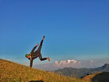 Low angle view of man exercising on mountain against blue sky