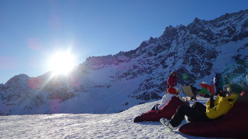 People sitting on snowcapped mountain against sky