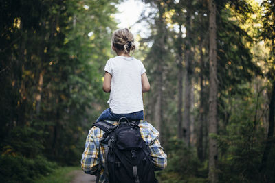 Rear view of father carrying daughter on shoulder while walking in forest