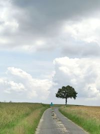 Road amidst trees on field against sky