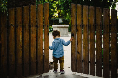 Rear view of boy standing by gate against fence