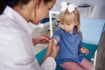 Doctor applying band-aid on girl's arm in medical practice