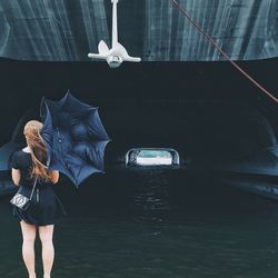 Rear view of woman holding umbrella standing against canal