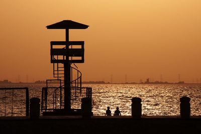Silhouette lifeguard hut on beach against orange sky