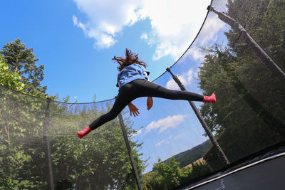 Low angle view of person jumping on tree against sky