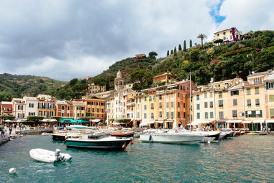 Sailboats moored on sea by buildings in city against sky