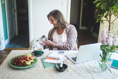 Smiling senior woman touching dog while working at table from home