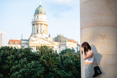 Side view of woman standing on column with concert hall in background