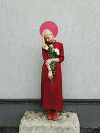 Woman holding bouquet while standing against wall