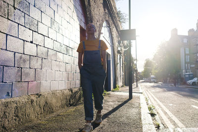 Young non-binary person walking with hands in pockets on footpath