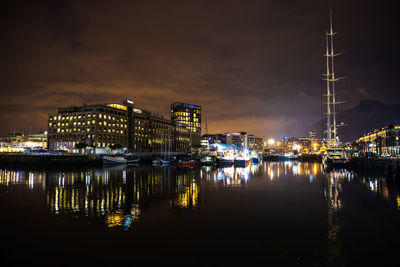Illuminated buildings by river against sky at night