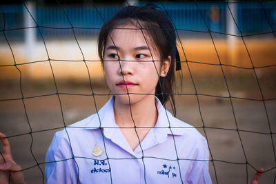 Thoughtful young woman standing behind net