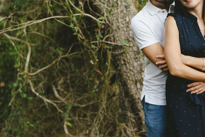 Midsection of couple standing against tree