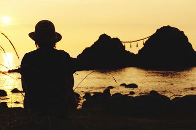 Silhouette men at shore against sky during sunset