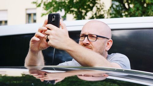 Close-up of man wearing eyeglasses using mobile phone by car