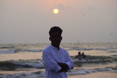 Rear view of man standing at beach against sky during sunset