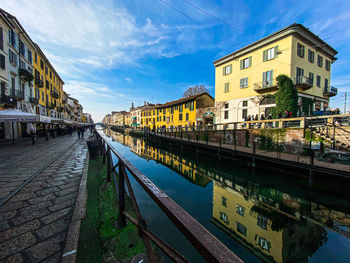 Canal by buildings in city against sky