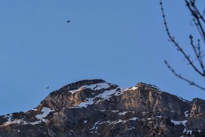 Low angle view of snowcapped mountains against clear blue sky